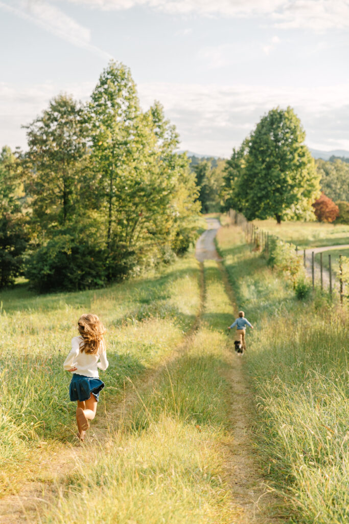 children running down grassy path with dog and mountains in the background, having fun exploring during a family photo session at the Biltmore Estate in Asheville, NC