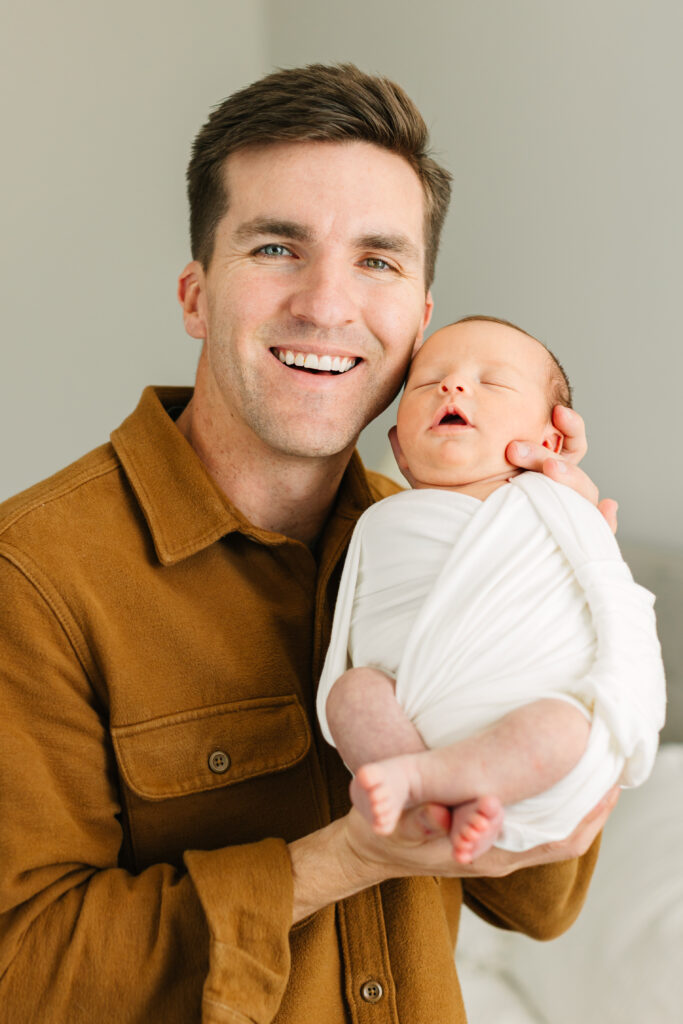 dad pictured smiling while holding his newborn son cheek-to-cheek