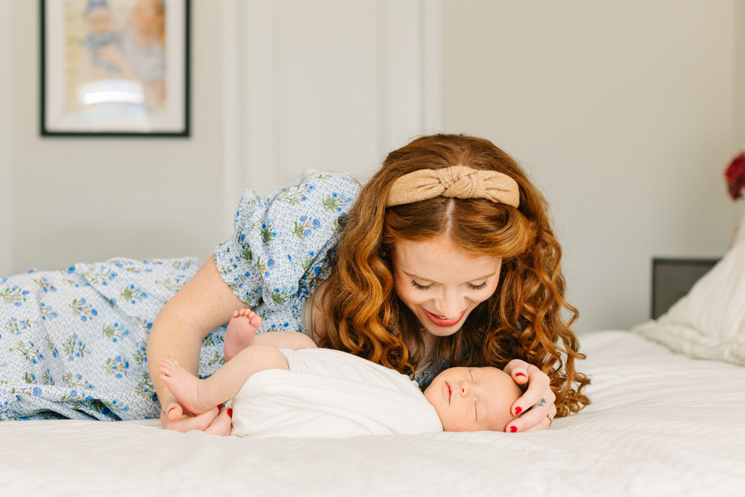 mom pictured smiling down at newborn while laying on bed