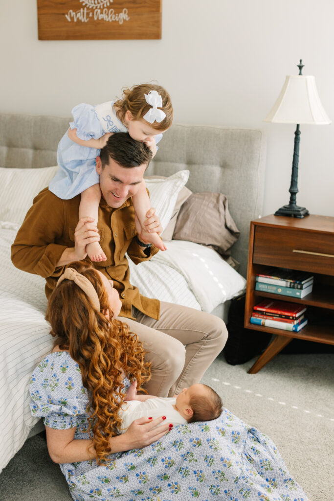 Family smiles at each other while sitting on bed during In-home newborn family photos in Asheville, NC with newborn photographer Rachel Marie Photography
