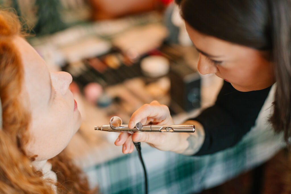 Close up photo of mom getting her makeup airbrushed on by makeup artist.
