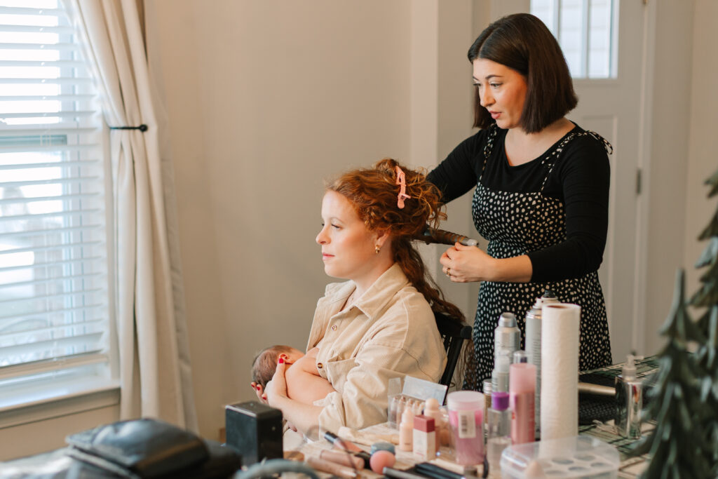 Newborn mama sitting in chair, feeding her baby, while getting hair done. 
