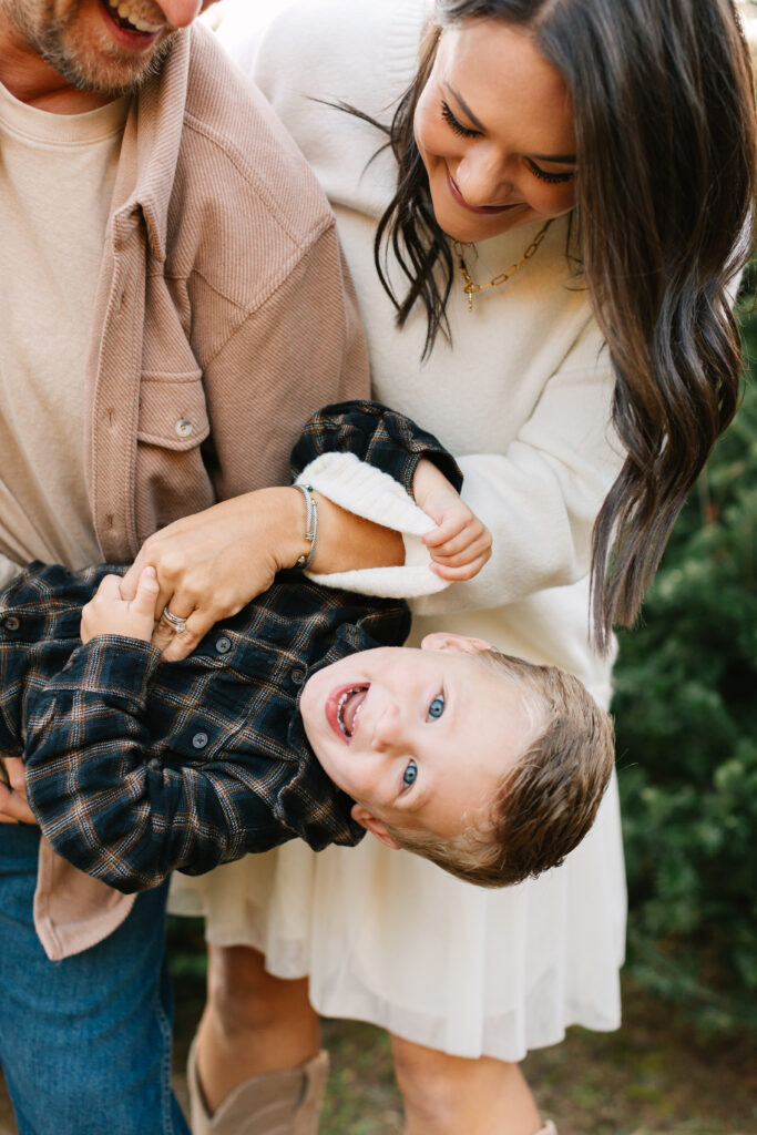 Little boy upside down, laughing with mom and dad at a Christmas tree farm during family photos with Asheville Family Photographer