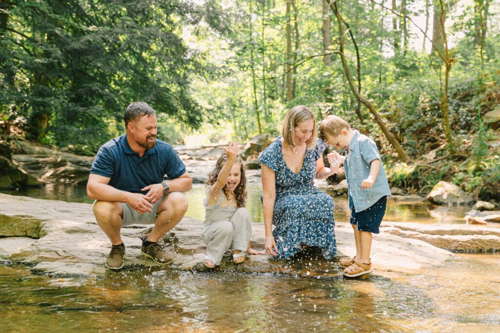 a mom, dad, daughter and son splash together in a river during river family photo session in Asheville, NC