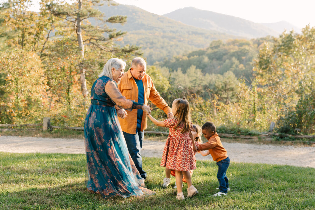 Grandparents play with grandchildren holding hands and smiling during extended family photo session in Asheville, NC with family photographer Rachel Marie Photography
