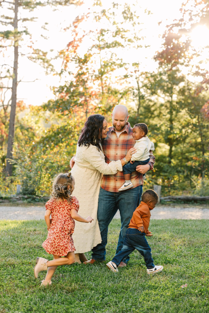family plays in a grassy field together while kids run around them during extended family photo session in Asheville, NC with family photographer Rachel Marie Photography
