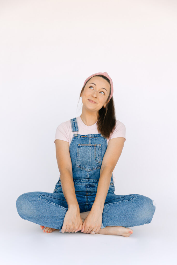 Asheville photographer, Rachel Marie Photography dressed up as Ms. Rachel, sitting criss-crossed and looking up to the right while smiling.