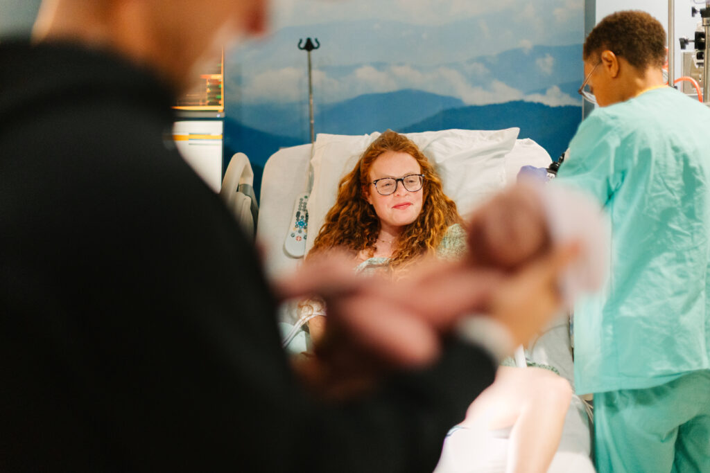 father holds newborn son in Hospital room at Mission Hospital in Asheville, NC while new mom looks on during birth photography session with Rachel Marie photography