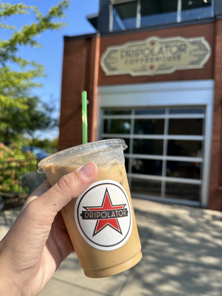 Hand holding Iced coffee in front of Dripolator Coffee House in South Asheville, NC