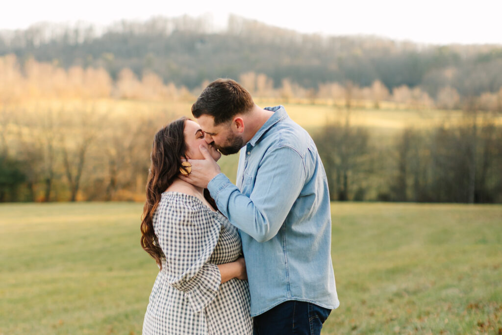 Pregnant couple kisses in a field with mountain views during maternity photo session with Asheville Maternity Photographer Rachel Marie Photography