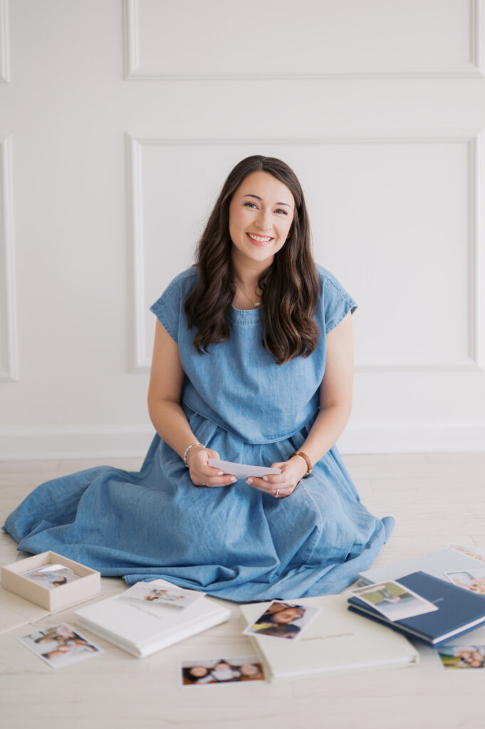 Photographer sits on floor with photo albums and printed photos all around her to showcase the print products she provides for her family photography clients in the asheville, nc area