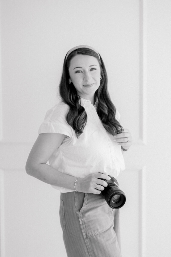 A family photographer who is great with young kids holds her camera and smiles during her own branding session to showcase her own family photographer business in Asheville, NC
