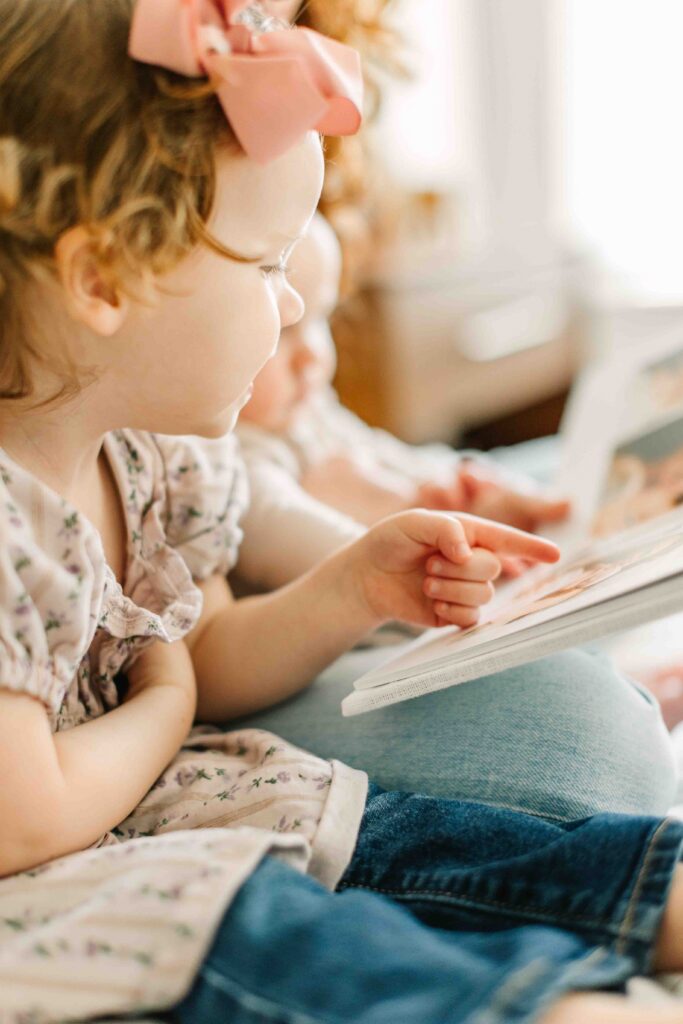 Little toddler girl smiles and points at a photo of her family printed into a family photo album designed by Asheville Family Photographer, Rachel Marie Photography