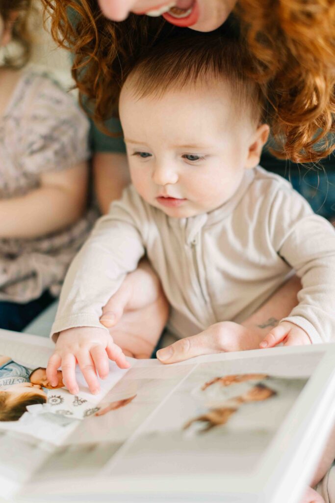 Baby boy sits in mom's lap and looks at a photo of his family printed into a family photo album designed by Asheville Family Photographer, Rachel Marie Photography