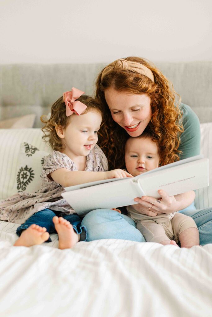 Little toddler girl smiles and points at a photo of her family printed into a family photo album designed by Asheville Family Photographer, Rachel Marie Photography