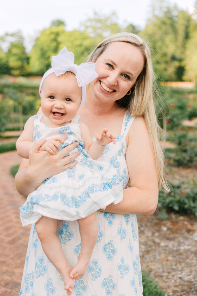 mom holds smiling baby daughter in matching dress in the rose gardens at the biltmore estate in asheville, nc during family photoshoot