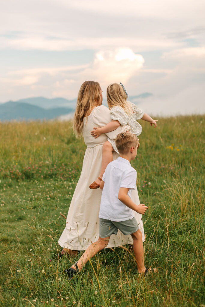 Mom carries daughter and walks with son at family photo session at Max Patch, NC with Asheville Family Photographer Rachel Marie Photography
