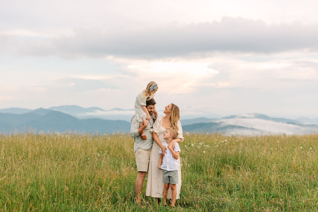 Family stands together in grassy field overlooking blue ridge mountains on a cloudy evening at Max Patch near Asheville, NC with family photographer Rachel Marie Photography