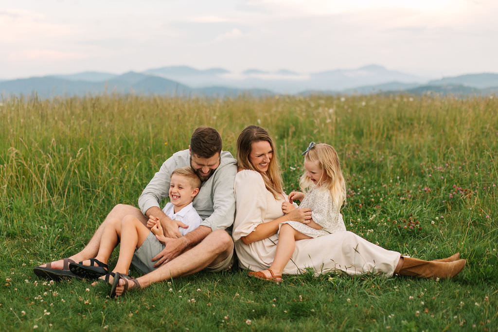 Family sits in grass and tickles each other at family photo session at Max Patch, NC with Asheville Family Photographer Rachel Marie Photography