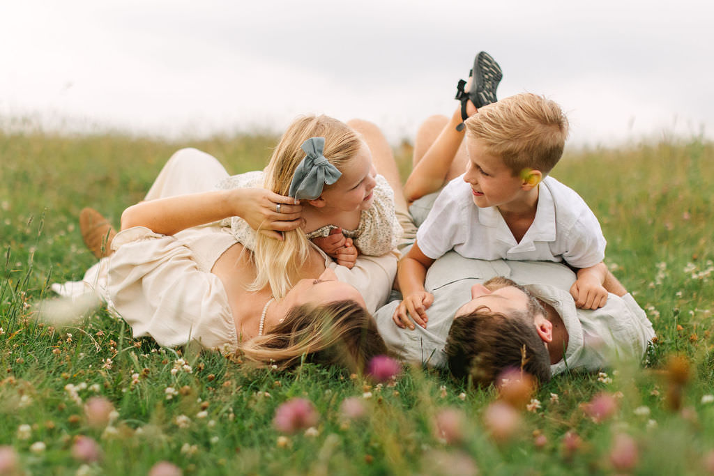 Family lays together in grassy field on a cloudy evening at Max Patch near Asheville, NC with family photographer Rachel Marie Photography